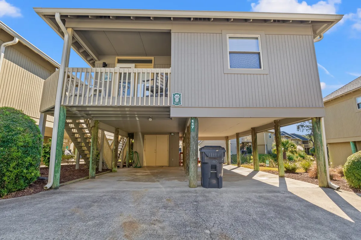 An elevated porch supported by sturdy pillars overlooks green landscaping, providing a shaded space for outdoor dining or relaxing with family. The airy design and serene surroundings reinforce the cottage's blend of privacy and connection to nature.