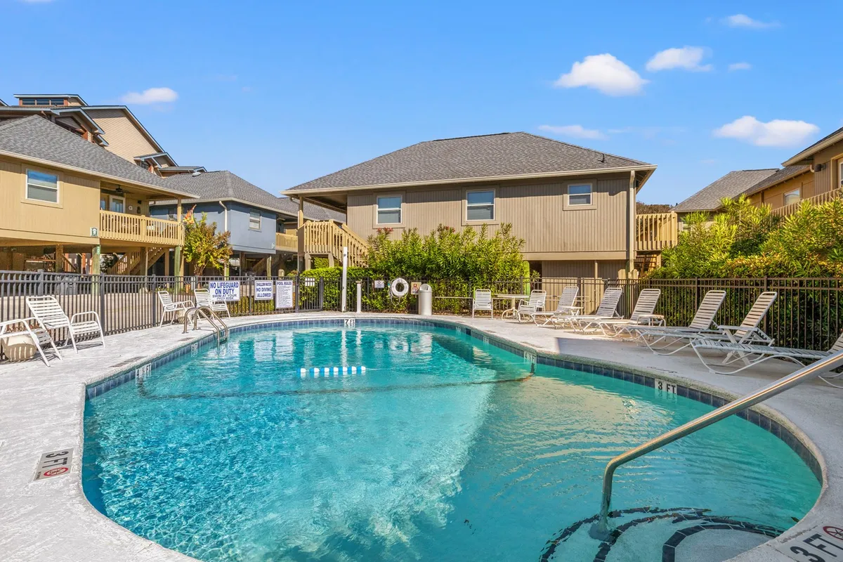 The image showcases an inviting swimming pool lined with comfortable lounge chairs, perfect for relaxing under the South Carolina sun. In the background, charming cottage-style buildings are visible, and the scene captures guests enjoying a laid-back atmosphere—children playing, friends chatting poolside, and the warm glow of the early evening.