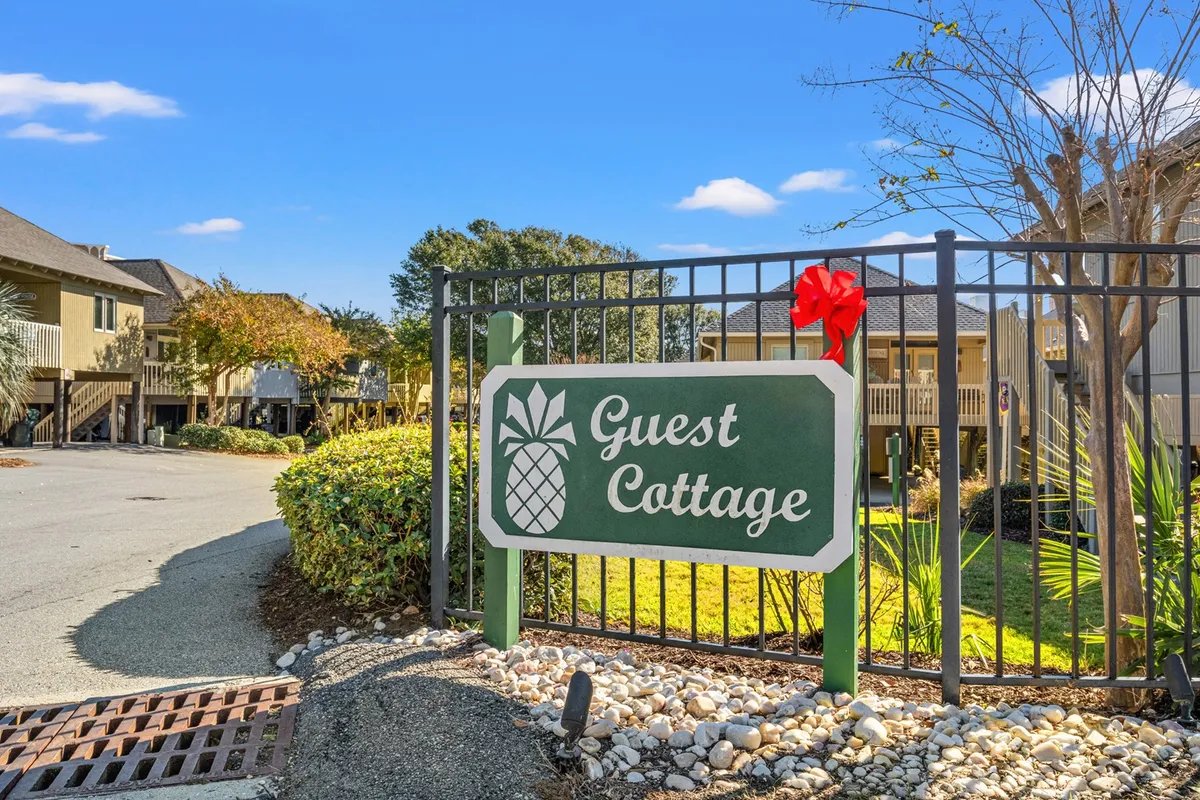 The inviting entrance to Guest Cottage is marked by a welcoming sign with a pineapple motif and a beautifully landscaped garden. Guests are shown enjoying the communal outdoor space, hinting at opportunities for socializing and connecting with others within the vacation complex.