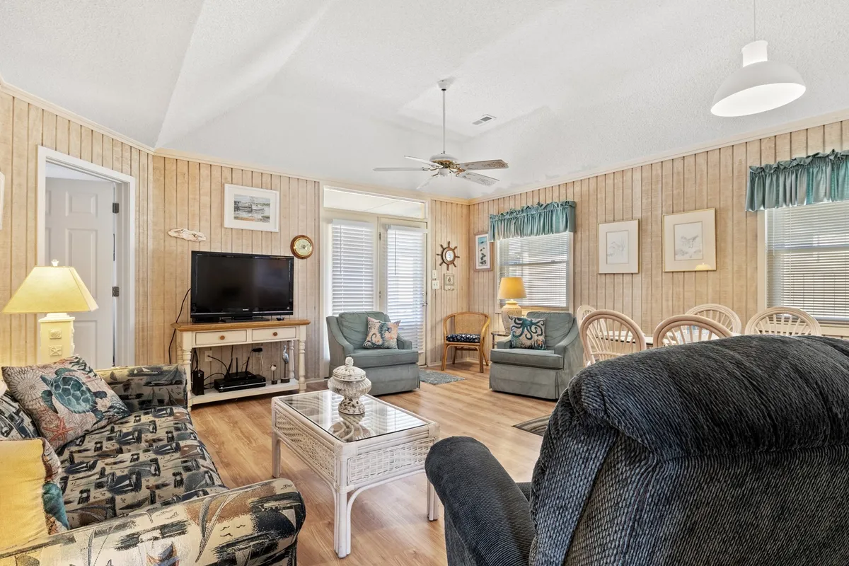 A cozy living area features a patterned sofa, centered coffee table, and a television set, all arranged to promote easy conversation or movie nights. The room feels intimate and inviting, well-suited for relaxing evenings or lively family gatherings.