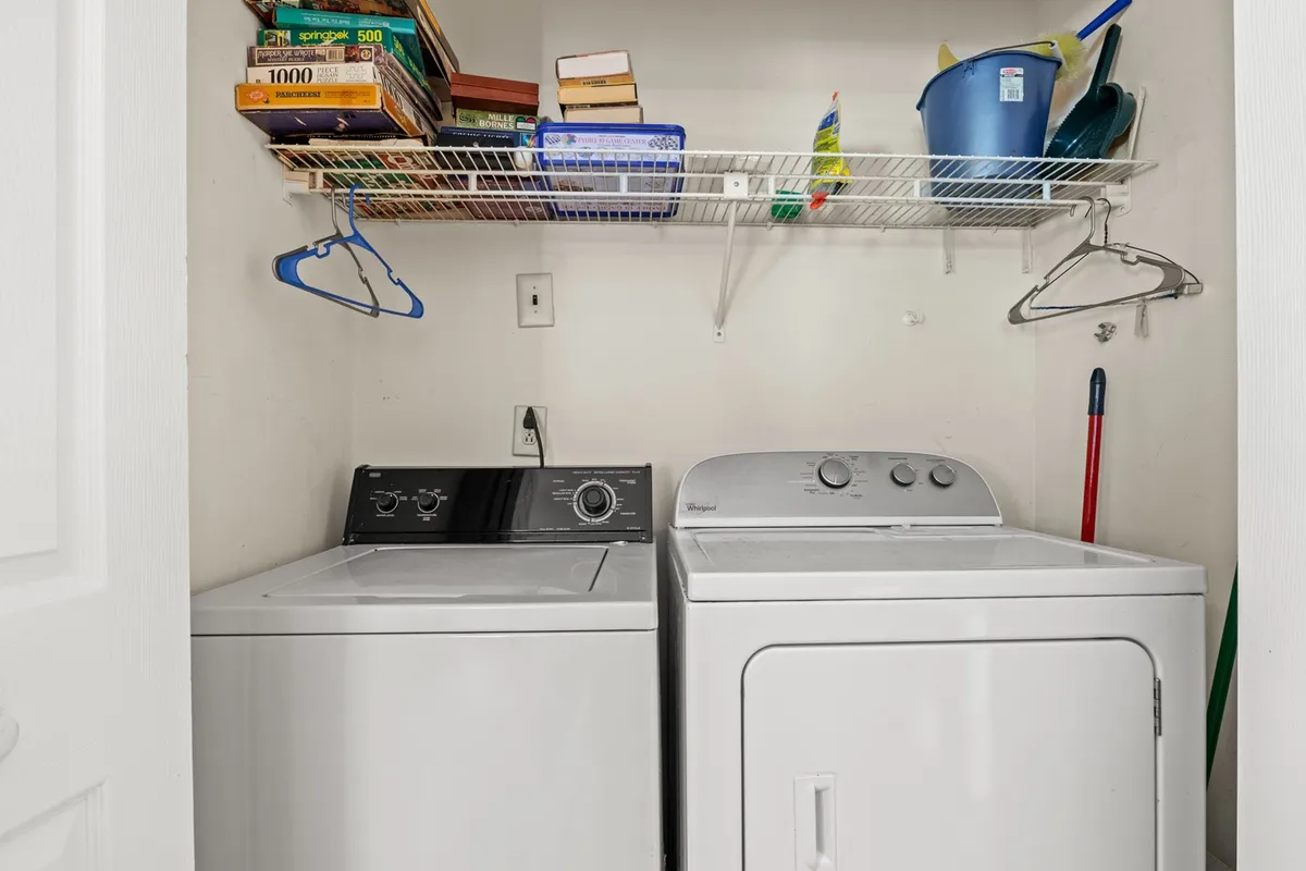This image depicts a practical laundry area featuring a washing machine, dryer, and a shelf with household items. The space is tidy and organized, making laundry tasks convenient for guests.