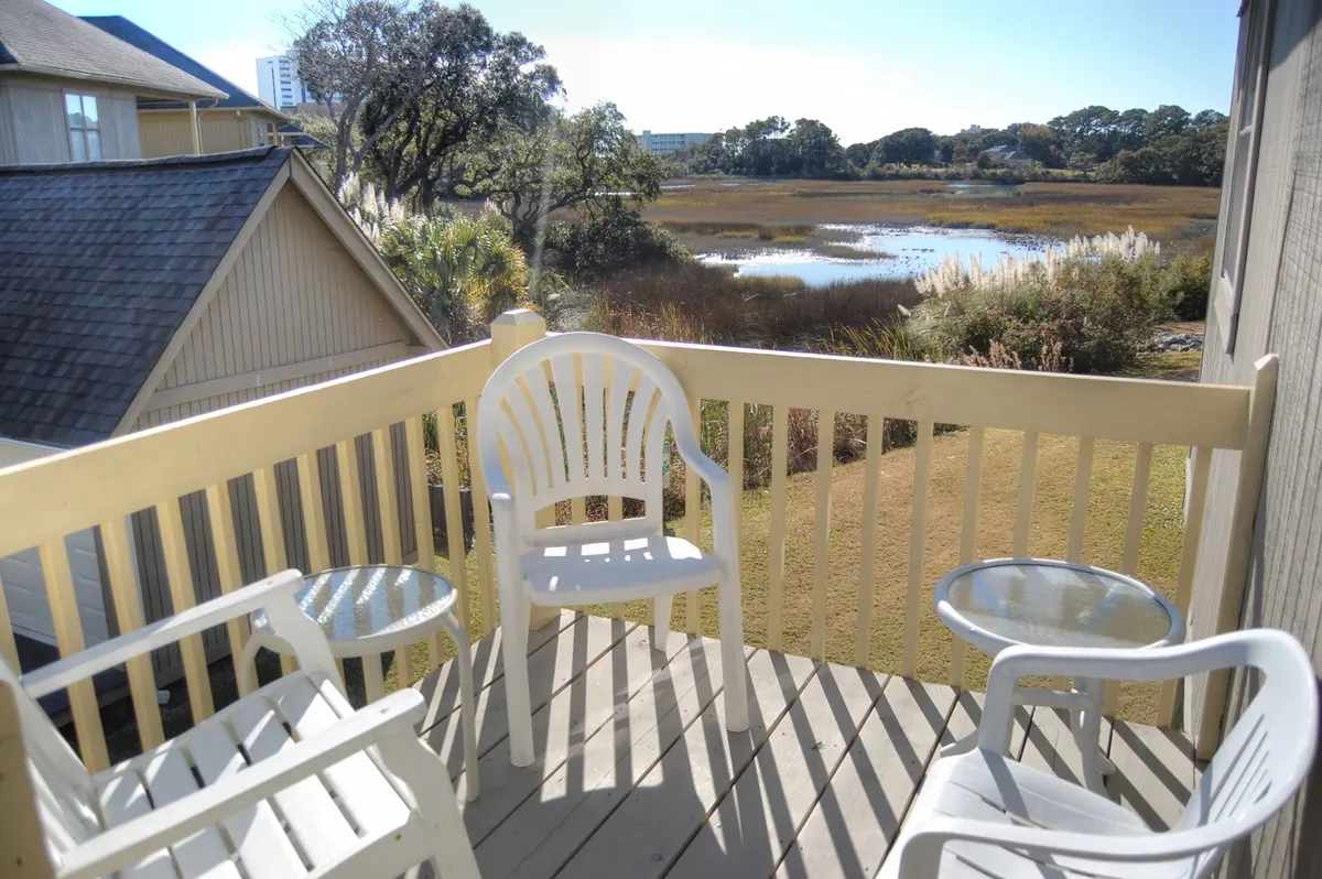 A private balcony with comfortable chairs overlooks a serene expanse of marshland, offering a peaceful spot to enjoy morning coffee or observe wildlife. The view captures the natural surroundings and tranquil atmosphere, with soft sunlight streaming in and hints of the cottage's privacy.