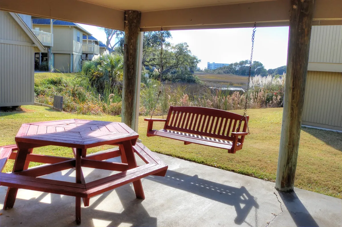 A lush outdoor area featuring a wooden swinging bench, a picnic table perfect for gatherings, and expansive greenery leading to a water view. The inviting setup signals a welcoming environment for family relaxation after a day of adventure.