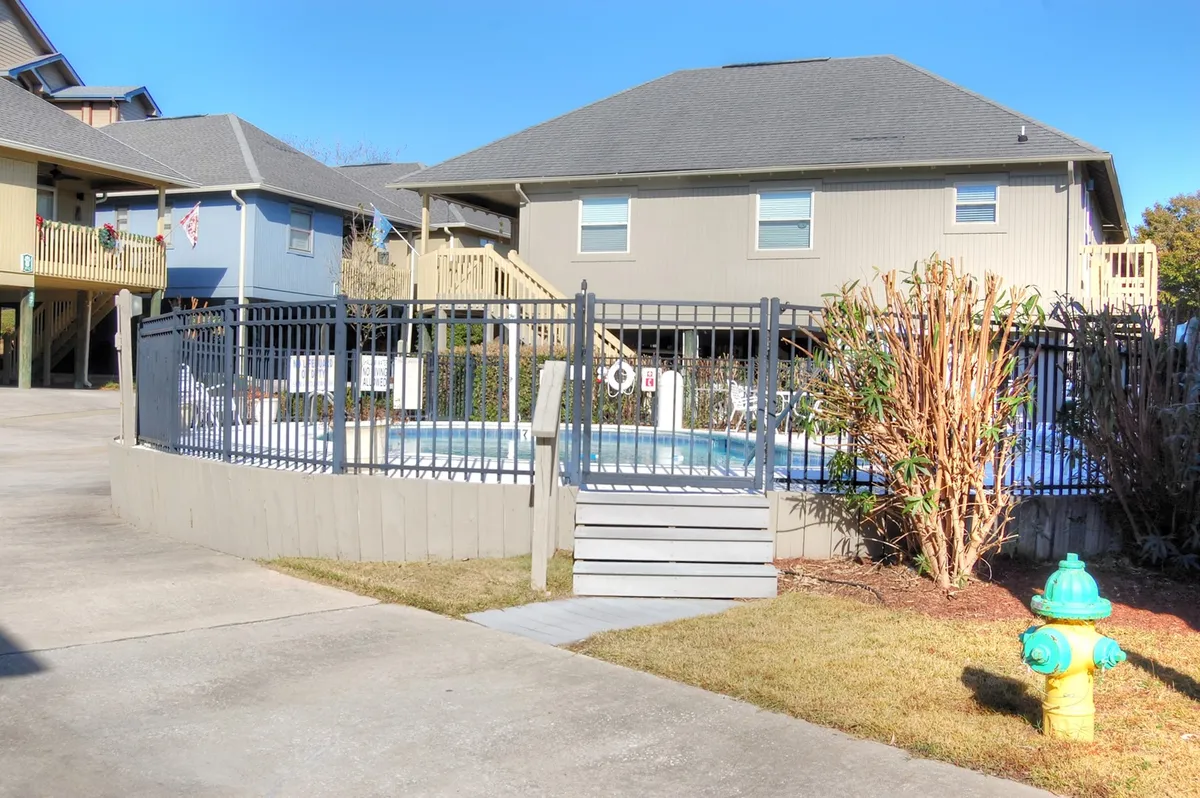 A sparkling community swimming pool is surrounded by a fenced area and lush landscaping. Stairs lead down to the pool deck, where lounge chairs invite sunbathing and social gatherings. The inviting scene hints at the resort-style amenities available to guests.