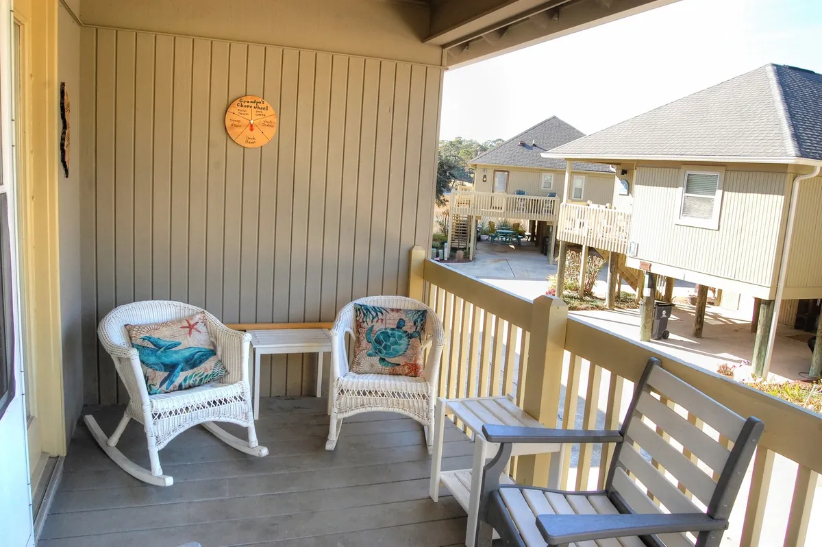 This image captures the exterior porch area of the guest cottage, featuring inviting rocking chairs, a small side table, and a decorative wall plate. The overall scene is peaceful and encourages relaxation while taking in the neighborhood ambiance.